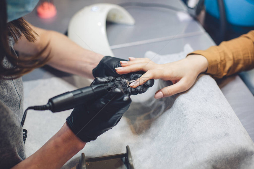 特写专业美容师手在客户指甲上使用电钻文件应用人造指甲的程序手用工具的美甲师美甲师手图片