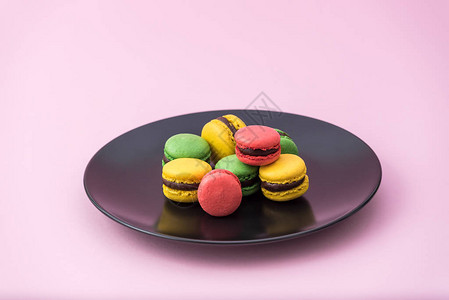 粉红色柔和背景的黑色盘子里的美味法国马卡龙红色黄色图片