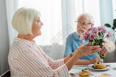 高年男子在厨房早餐时给微笑的妻子送花束的选图片