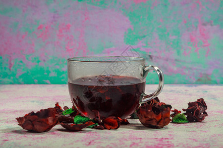 在玫瑰花瓣和干茶果酱之间在一个木制桌上的玻璃杯子里喝红图片