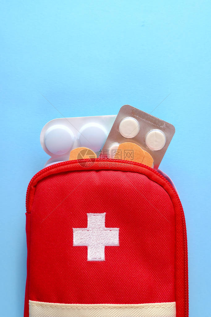 药丸和粘合绷带从开放的红色旅游急救箱中伸出来图片