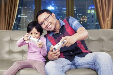英俊的亚洲男人晚上在家庭房间里和女儿欢快热情地玩电图片