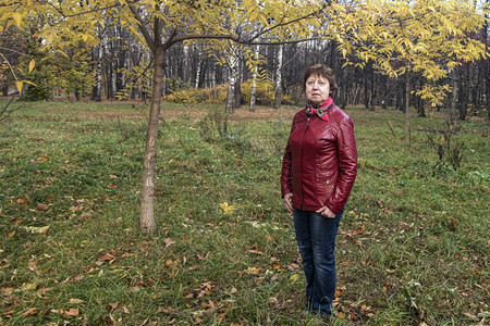 秋穿红色皮夹克的女士站在山灰黄色背景图片