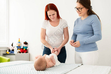 女按摩治疗师教年轻母亲如何对新生儿男孩进行按摩婴儿按摩概图片