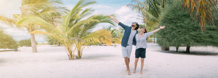 一对恋人正在热带海滩上散步一个男孩和一个女孩在热带植物和棕榈树之间的沙滩上行走新婚夫妇享受图片