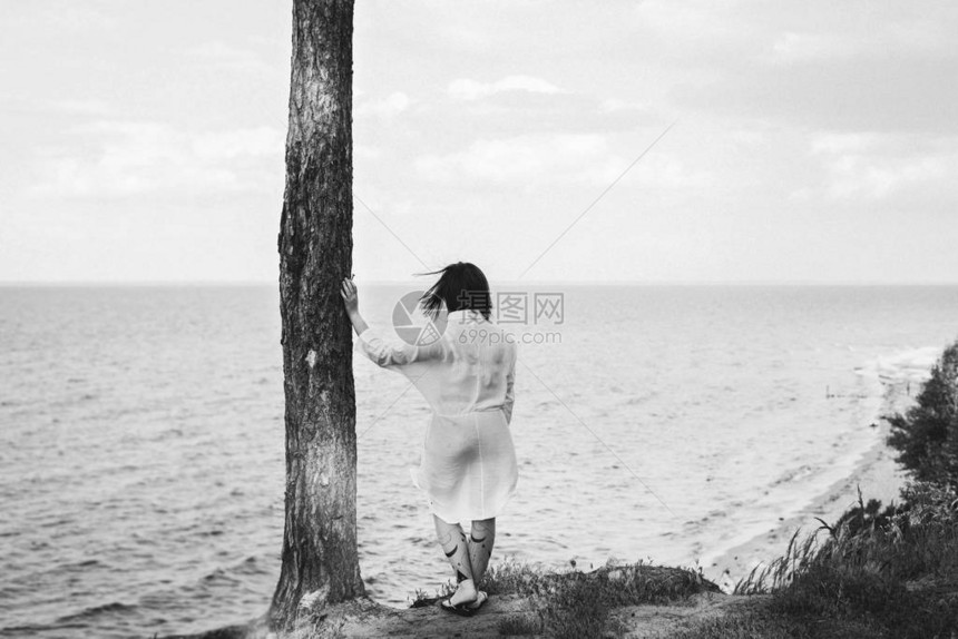 身着白裙子的女人站在松树上看着大海后视线地平线可图片
