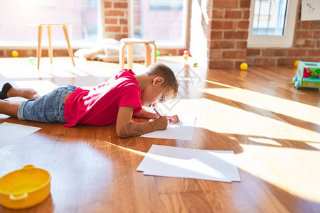 在幼儿园用纸和铅笔坐在地板上画围着许多玩图片