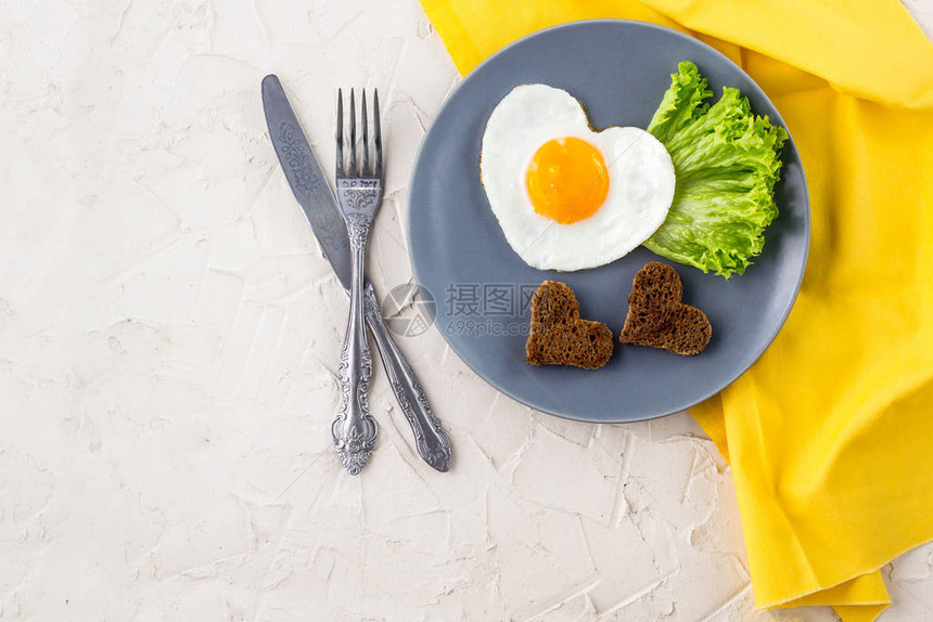 白盘和黄餐巾纸上配有心形炸鸡蛋的情人日早餐图片