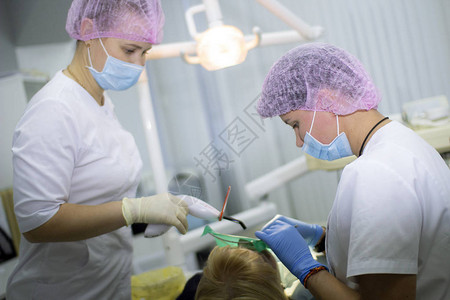 一名穿白制服的女牙医及其助理对病人进行检查医学牙科图片
