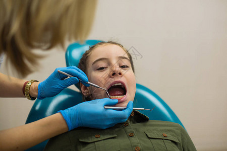 在牙科诊所对小女病人进行牙齿检查的牙科医生图片