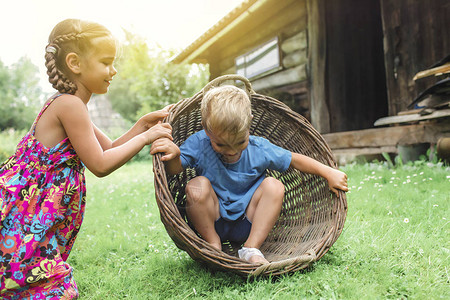 可爱的小男孩和女孩在夏天在村庄的旧乡间别墅后院玩跨栏篮图片