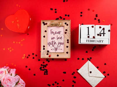在红色框架中的情人节快乐问候平躺着红心纸屑木制日历信封心形礼盒永图片