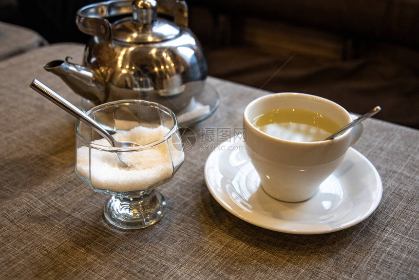 泡茶用的金属茶壶白陶瓷杯咖啡馆桌上的图片