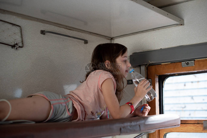 火车上的女孩拿着一瓶水乘坐旧火车的女孩附近有一瓶水一个9岁的女孩在火车上用塑料瓶喝水消图片