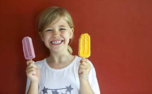 在红色背景上吃冰淇淋的金发小女孩图片