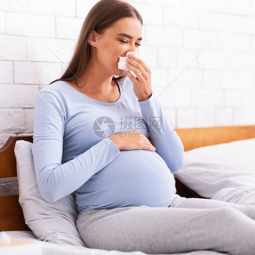 生病的孕妇在床上睡觉时打喷嚏并用纸巾手帕抽鼻涕图片