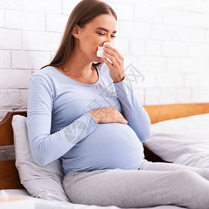 生病的孕妇在床上睡觉时打喷嚏并用纸巾手帕抽鼻涕图片
