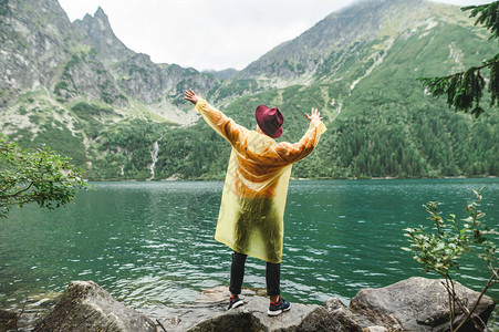 一个穿着黄色雨衣和帽子的时尚男人的肖像站在湖边的岩石上图片