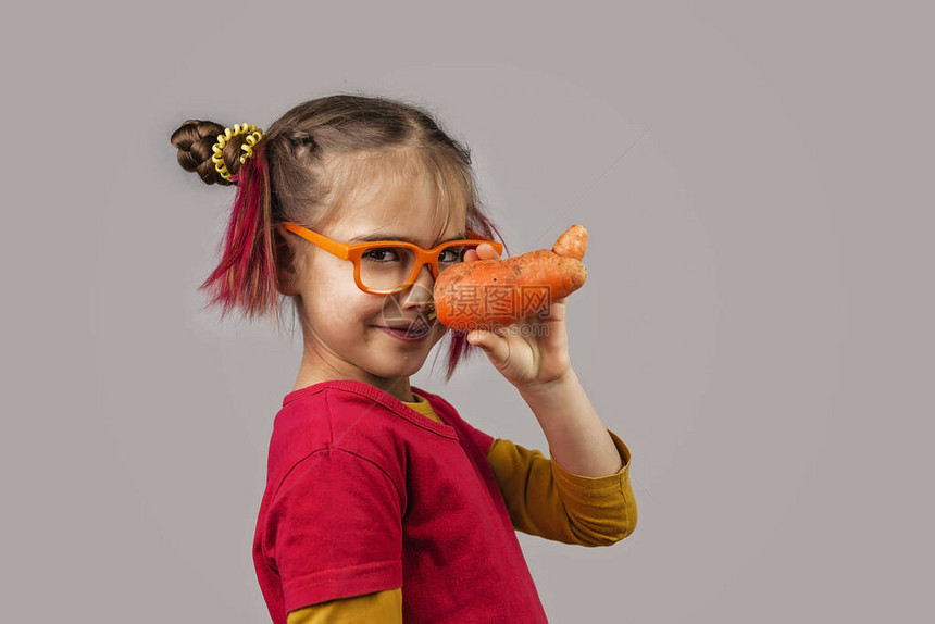 戴着眼镜的小头发怪异的孩子拿着畸形的错误颜色的水果和蔬菜图片