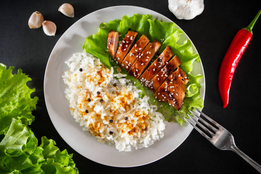 白盘上配有芝麻种子生菜和大米的Teriyaki鸡图片
