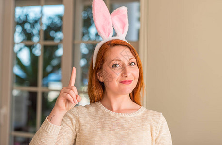 在家戴着复活节兔耳朵的红发女人惊讶地发现一个想法或问题图片