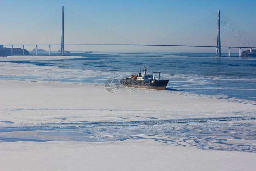 大海被冰雪覆盖海湾里有一艘船远处一座现代化的大型桥梁横跨海峡图片