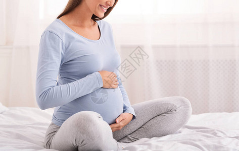 无法辨认的怀孕女孩坐在温床和舒适的卧室里图片