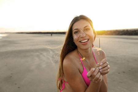 快乐开朗的女孩在日落时分在海滩上举着孟加拉灯漂亮的微笑女人在海滩图片