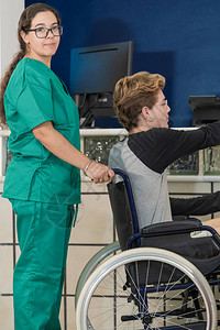 漂亮的护士一边帮助坐在轮椅上的年轻人一边看着镜头图片