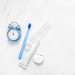 白色大理石桌子背景上带有蓝色闹钟的牙齿卫生和口腔牙科护理产品图片