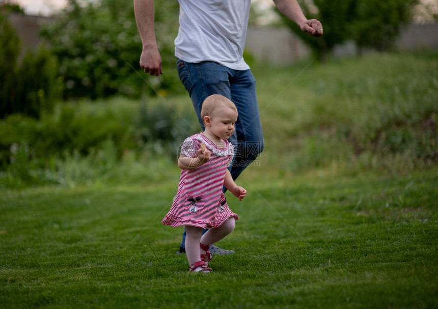 小孩1岁的女婴去父亲带着孩子穿过绿草婴儿在父母的支持下学会走路1岁的女孩和爸生活方图片