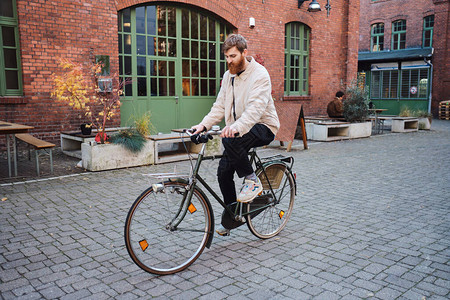 年轻迷人的休闲男人若有所思地骑着旧经典自行车穿过舒图片