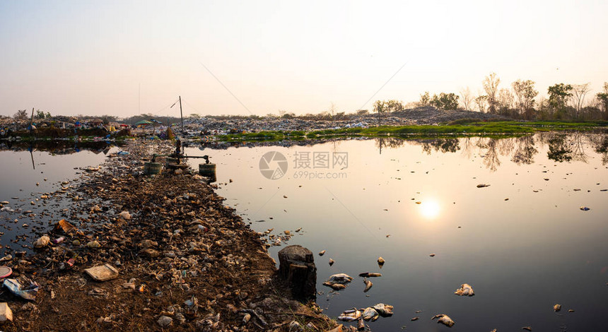 污染的水和山大垃圾堆和太阳的污染在背景中落下图片