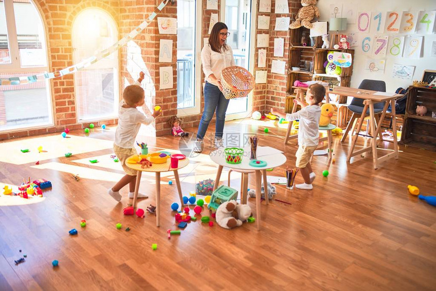 漂亮的老师和幼儿在幼儿园的许多玩具周围用球和图片