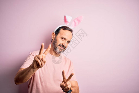 中年白发男子戴着耳朵站在孤立的粉红色背景上图片
