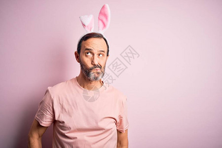 穿着兔子耳朵的中年男子站在孤立的粉红色背景上图片