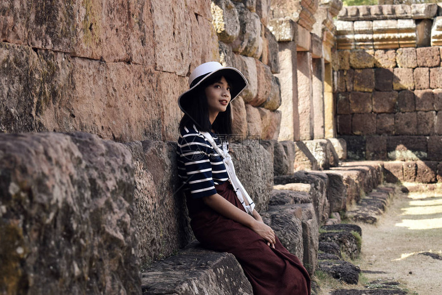 身着条纹衣服白帽子的年轻漂亮的亚洲女孩坐在一个古老的兴都寺庙废墟的地图片