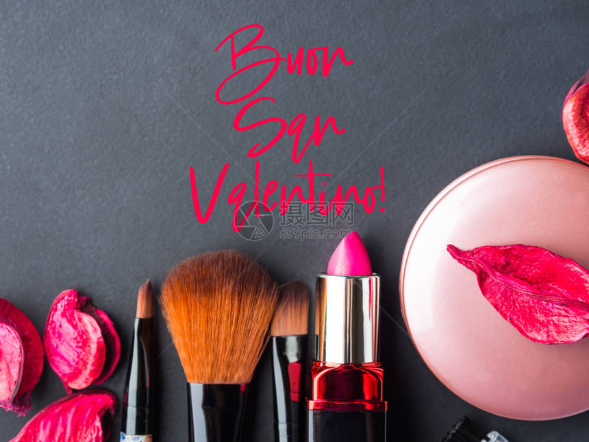 用黑色背景上的粉红色花瓣化妆产品口红腮红和工具刷女人配件意大利语的情人节快乐问候带图片
