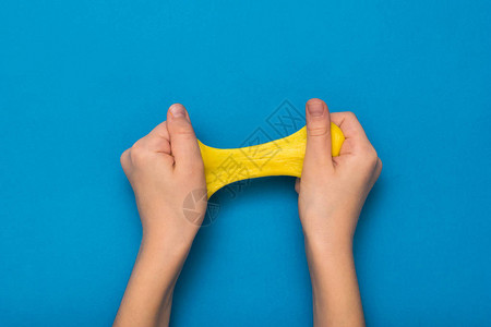手和蓝色背景上的亮黄色粘液玩具抗压用于开发手部运图片