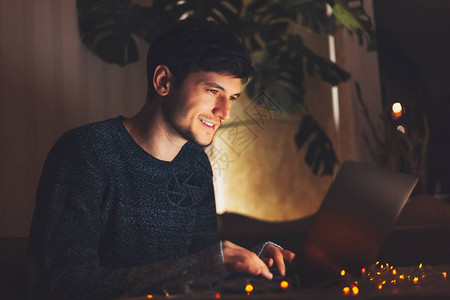 年轻快乐的小伙子在暗房里工作在笔记本电脑上做夜间肖像家里图片