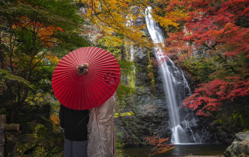日本大阪秋红黄背景箕面瀑布公园红桥上日本夫妇和图片