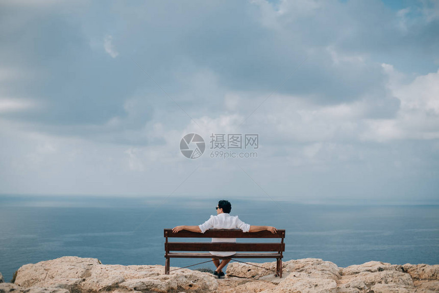 一个男人坐在岩石上的长椅上图片