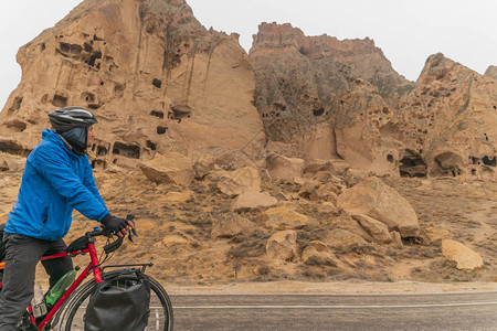 男骑着自行车站立在土耳其Selime的岩石构造中图片