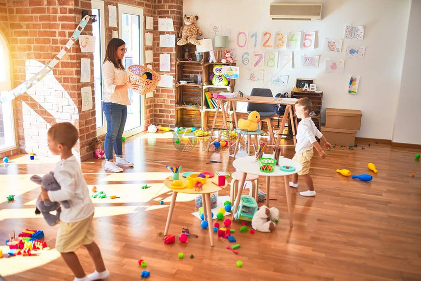 漂亮的老师和幼儿在幼儿园的许多玩具周围用球和图片