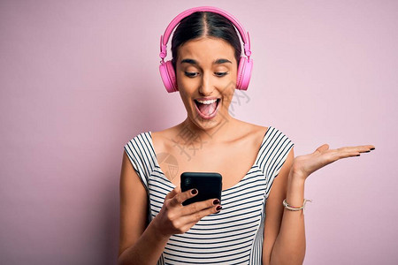 用耳机和智能手机听音乐的黑发美女非常高兴和奋图片