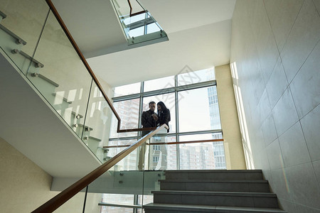 两名身穿正式服装的年轻同事站在当代大型商业中心内各楼梯之间的图片