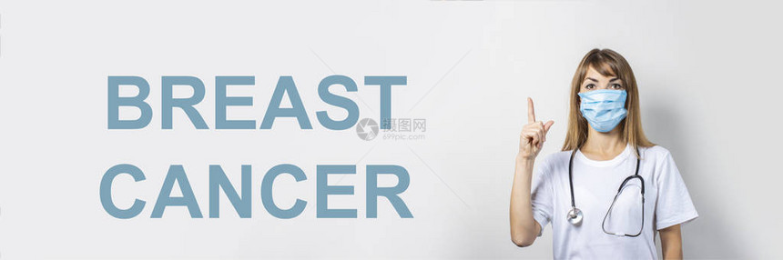 戴着医用口罩和听诊器的年轻女子用手指着浅色背景添加了乳腺癌一词横幅医生理念图片