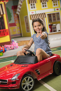 快乐的小微笑女孩坐在室内的玩具车上可爱的孩子在游戏室竖起大拇指孩子们图片