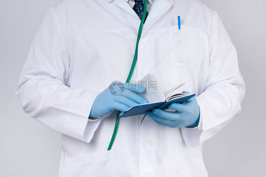 身穿白大衣和蓝色手套的医生拿着蓝纸笔记本做笔记图片