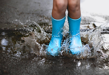 穿着蓝色雨靴的孩子跳进水坑关闭你图片